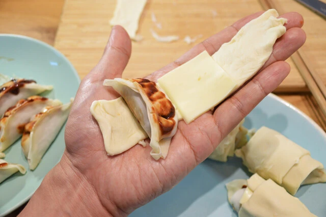 (2)包む! あらかじめ解凍しておいたパイシートとチーズを餃子が包めるくらいにカットし、餃子とチーズをクルクルと包むように丸めていく。クロワッサンのような見た目になればOK