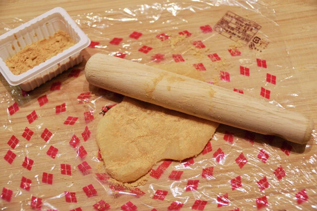 （１）のばす！　まな板の上に信玄餅の包装ビニールを敷き、その上に信玄餅を４、５個並べる。餅にきなこをまぶしながら、のし棒を使って全体をくっつけながら薄くのばしていこう