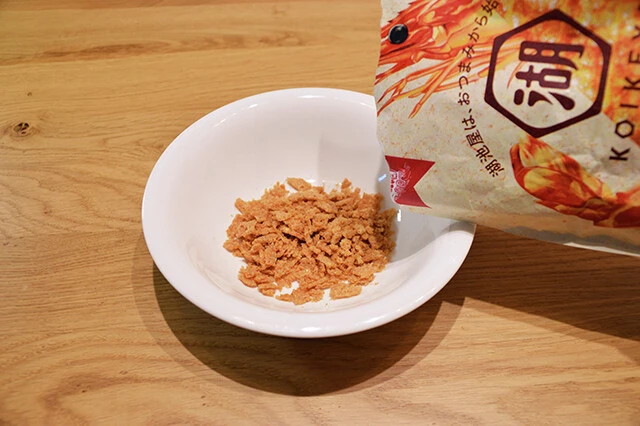 (1)砕く! 「KOIKEYA The 海老」の袋を軽く開け、空気が通る状態にしてから豪快に握り潰してスナックを粉砕する。粉々にできたら浅めの食器に移し、砕ききれてない部分をさらに潰す