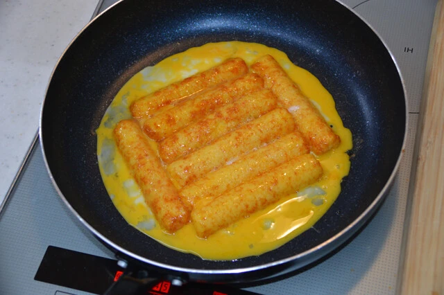 縦にスライスしたうまい棒テリヤキバーガー味に溶き卵を吸わせ、フライパンで焼く。焼けたら焼きそば、キャベツを上にのせ、ソース、マヨ、青のりをかければ完成