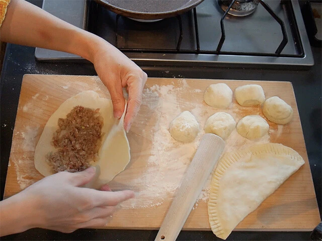 ４．生地の上に半月型に薄くタネを塗り半分に折り畳み、端を指やフォークの先などで押してくっつける。（大きく平たい餃子を作るようなイメージ）