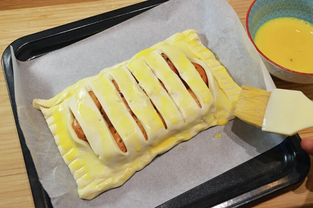 （２）閉じる！　もう１枚のパイシートに包丁で切り込みを入れ、（１）の上から重ねたら生地の端の部分をこねて合体させよう。表面には水を加えた卵黄を薄く塗ると見た目がウマそうに仕上がるぞ