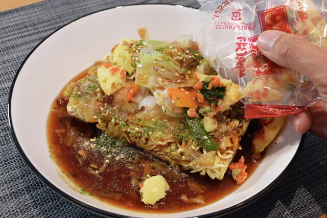 （４）仕上げ！　どん兵衛の天ぷらを袋のまま砕き、開封して全体に振りかける。さらにペヤングのふりかけとスパイスも振りかけたら完成。あんかけをたっぷりと絡めながら食べ進めよう