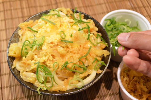 (4)仕上げ! 仕上げに丸亀製麺でテイクアウト時にもらえる青ネギと天かすを振りかけたら完成。卵が固まりすぎた場合は上からさらに溶き卵を少し回しがけすれば見た目が鮮やかになる