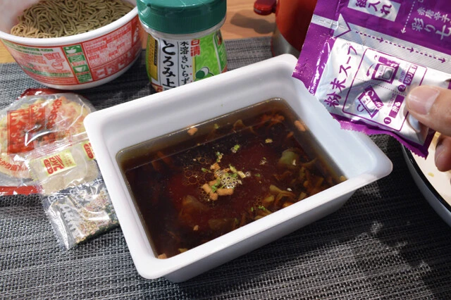 （２）混ぜる！　かやくと液体ソースを入れたカップに熱湯を注ぐ。量は線の半分くらいが目安。さらにどん兵衛の粉末スープも３分の１から半分程度入れ、よくかき混ぜたら鍋に移す