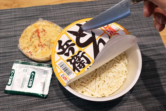 (1)刺す! どん兵衛かき揚げ天ぷらうどんのフタを開けたら粉末スープとかき揚げを取り出し、フタに包丁などで湯切り用の穴を開ける。お子さまがやる場合は扱いにくれぐれも気をつけよう