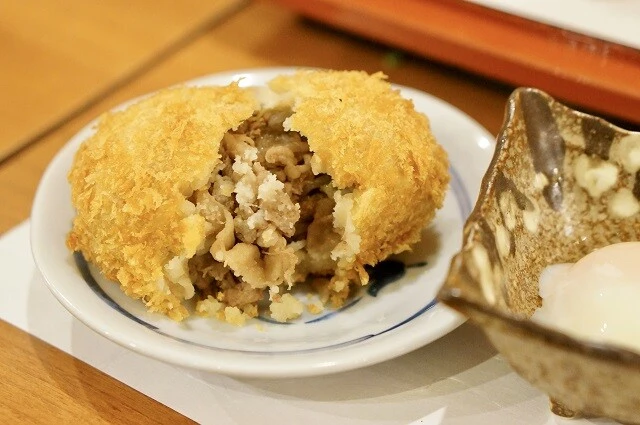 コロッケを割ると、中から「すき焼き」が現れる。温泉卵につけていただく