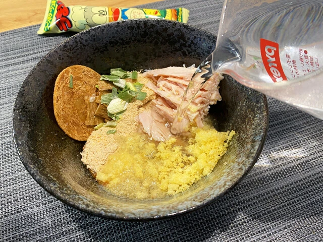 (3)つけ汁! 深めの食器にかやく、粉末スープ、液体スープ、細かくほぐしたサラダチキン、粉々に粉砕したうまい棒を投入。熱湯250ミリリットルを注ぎよくかき混ぜる。味が濃い場合は熱湯を足そう