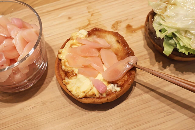 （２）のせる！　モスバーガーのダブルテリヤキバーガーを開き、スライスした岩下の新生姜を上側のバンズ（クラウン）にのせる。マヨネーズに貼りつけるようにのせると収まりがよい