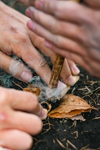 「キリモミ式火おこし」の様子。この方法で火をおこせるようになるまで2ヵ月かかったが、現在は1分で済むという