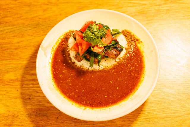 レバニラの上にはトマトとパクチーが。「シビ辛！レバニラカレー」のルーは麻婆のように赤みがかっている