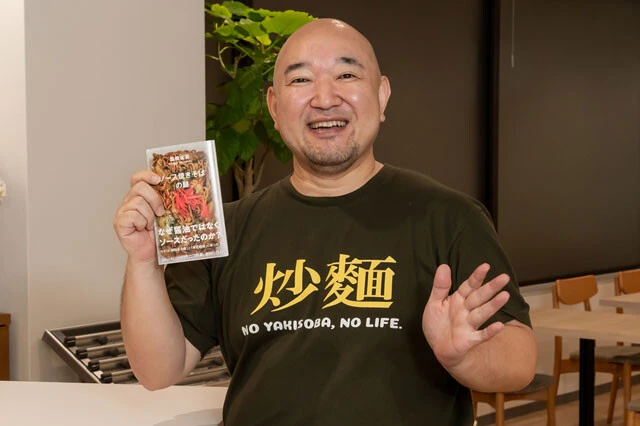 奥さんが誕生日プレゼントで作った「炒麺(チャーメン=焼きそば)Tシャツ」を着る塩崎さん。ちなみに裏には焼きそばのイラストともに「めちゃウメ~ん!」も文字がプリントされている