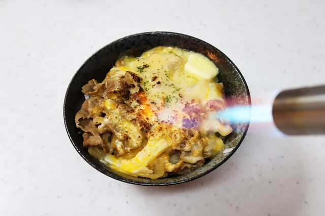 (2)バーナー! レンチンし終えたらガスバーナーでチーズをあぶって焦がしていく。この工程は省略しても問題ないが、チーズがさらに溶けてとろとろになり、香ばしさも増すのでオススメだ