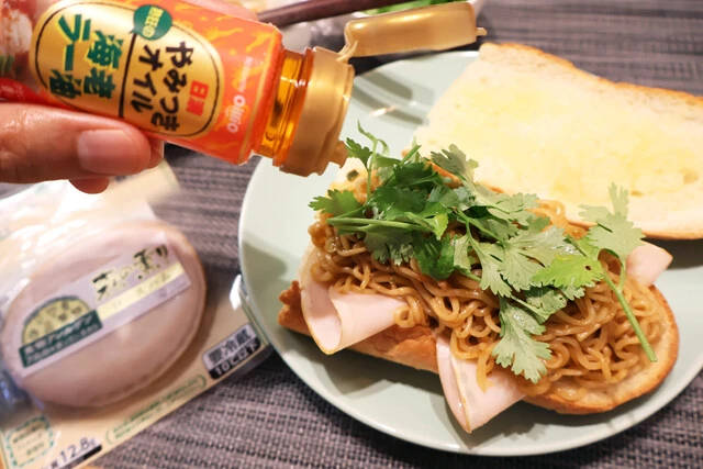 (4)仕上げ! 焼き上がったパンにハムをのせたら(3)とパクチーを盛り、やみつきオイル海老ラー油を垂らして、さらにパンをのせれば完成。こぼさないように押さえながら豪快にかぶりつけ!