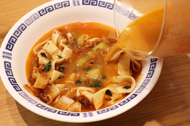 （３）スープ！　プチッと鍋の担々ごま鍋を熱湯150ミリリットルで希釈し、（２）に全量ぶっかける。そして麺を混ぜるようにしてほぐし、ビャンビャン麺のタレとスープを混ぜ一体化させよう