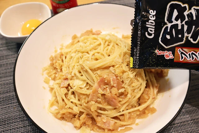 (4)仕上げ! パスタを盛りつけたら中心に少しくぼみを作り、そこに卵黄を落とす。仕上げに砕いた堅あげポテトのブラックペッパーと粉チーズを振りかければ完成。よく混ぜて食べよう!