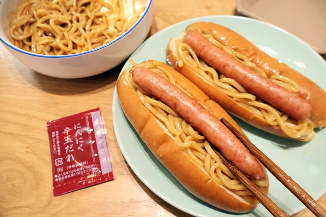 (3)挟む! ホットドッグ用のパンに(2)をたっぷりと挟み、さらにソーセージも挟む。調子に乗って麺を挟みすぎるとパンが裂けてしまう場合があるが、それでもOK! 包み紙を使おう!