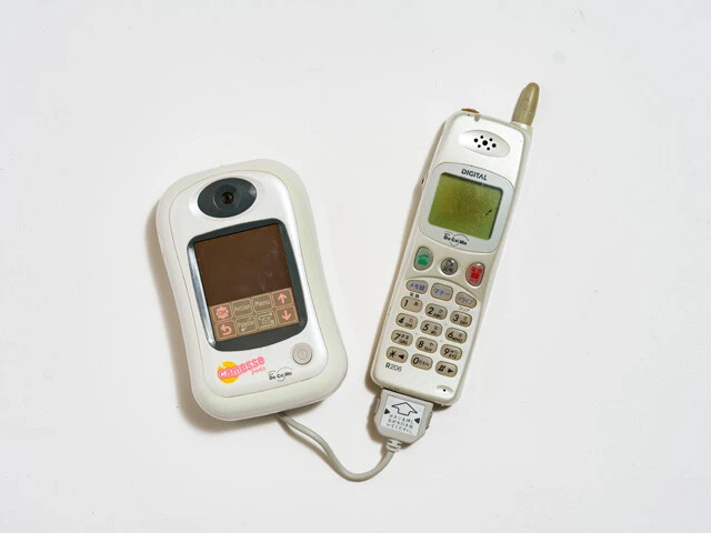 携帯電話に接続するカメラ付きメール端末キャメッセプチ。自撮りメインの内側レンズ、フレームが選べて付属タッチペンで落書きできるプリクラ仕様である。画像のメール送信も可。ほかに三菱電機「ラポッシュ」という端末も