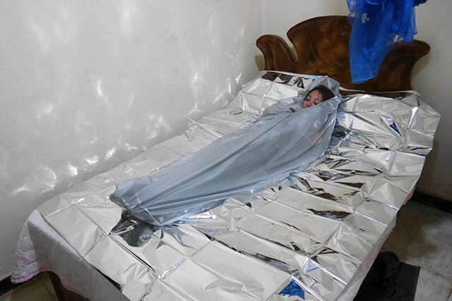 NASA開発の防寒用サバイバルシートと自転車の雨避けカバーに身を包む旅人