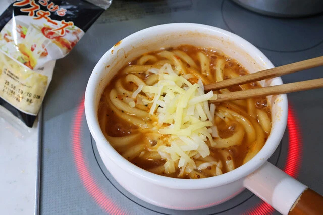 (4)チーズ! 麺がスープを吸収したら火力を弱め、とろけるチーズを適量入れる。ほんのり溶け始めたら火を止めて食器に移そう。スープをよく吸ったうどんは完全に極太生パスタ!