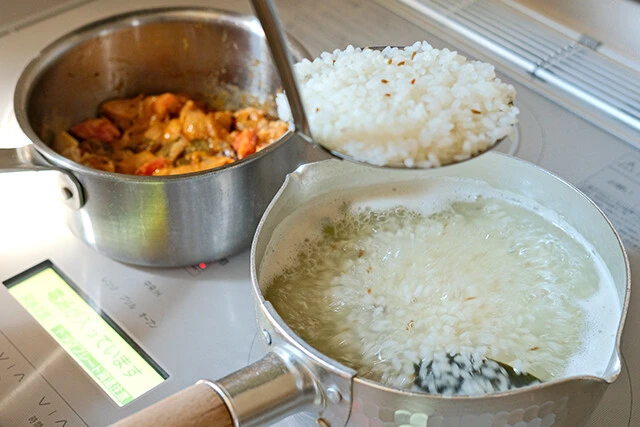 ゆでたコメをグレービーを入れている鍋に移すときは、利き手に網杓子を持ち、逆の手でグレービー入りの鍋を持つ。そして湯切りしながらコメを移す!