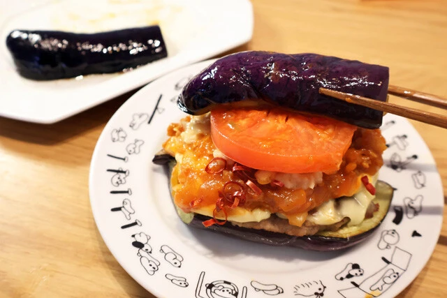 （４）仕上げ！　焼きナスの上にモスチーズバーガーの中身をのせ、その上にも焼きナスをのせれば完成！　ただし、そのままかぶりつくと確実に汁が垂れまくる。再び包み紙に戻して食べるとよい