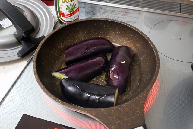 （２）蒸し焼き！　熱したフライパンにナスを並べ、オリーブオイルをたっぷりとかける。ナスが油を吸収したら水を少し垂らしてからフライパンにフタをし、蒸し焼きにしてしっかりと火を通そう