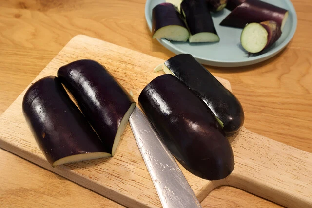 （１）切る！　ナスをバンズの代替で使うため、まずは縦半分にカット。その後、ふたつ合わせてバンズの形になるように細かくカットして形を整えよう。余った部分は漬物にでもするとよし！