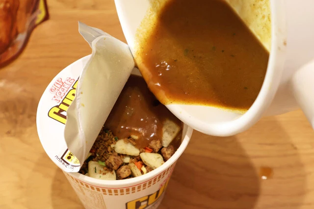（２）注ぐ！　カップヌードル カレーを開封し、（１）のスープのみを注いで3分待つ。注ぎにくい場合はカップを握って軽く麺を砕き、隙間をつくるとよい。スープが足りない場合は熱湯を足そう