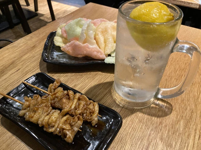 生搾りレモンサワー（88円）と、看板メニューの「名物　秘伝かわ串」（1本109円）。奥はお通しのえびせん