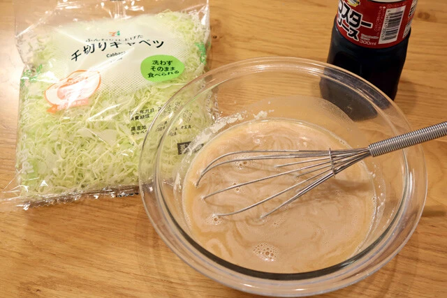 （２）生地！　薄力粉、ウスターソース、水をボウルに入れて泡立て器でしっかり混ぜる。薄力粉のダマがなくなったらキャベツも投入。キャベツはコンビニのパック野菜を使うと便利だ