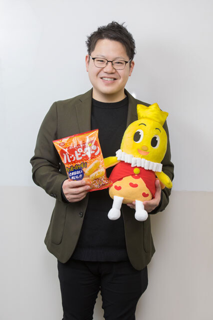 ハッピーターン担当の歴舎直輝さん。現在のハッピーターンはさまざまな改良が加えられて、常に進化を遂げているロングセラー。96g入り（参考小売価格248円・税込）がスタンダードで、79g入り、67g入り、28g入りや60g入りの4連商品もある