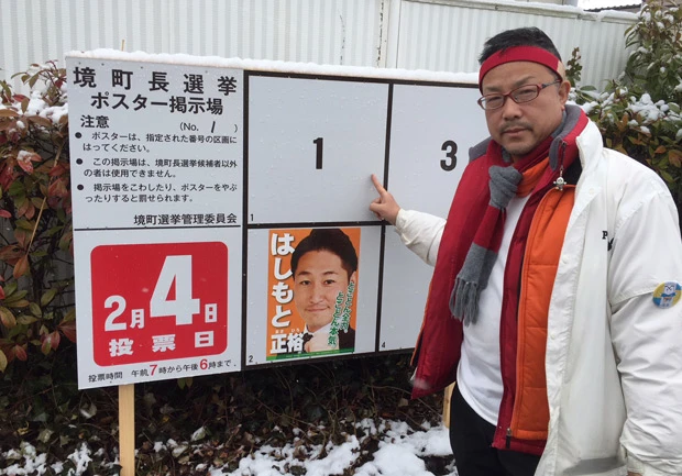  境町役場のポスター掲示板の前に立ち、自身の枠「１番」を指さす高嶋氏。ポスターは作らず、選挙運動もしなかった。