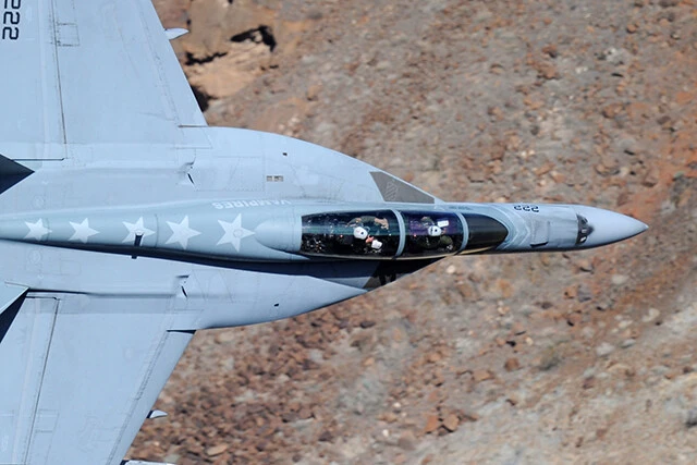 写真は複座２人乗りのＦ/Ａ-１８Ｆ。機体を真横にして細い谷間を抜ける。コクピット内に２人のパイロットが見える（撮影／柿谷哲也）