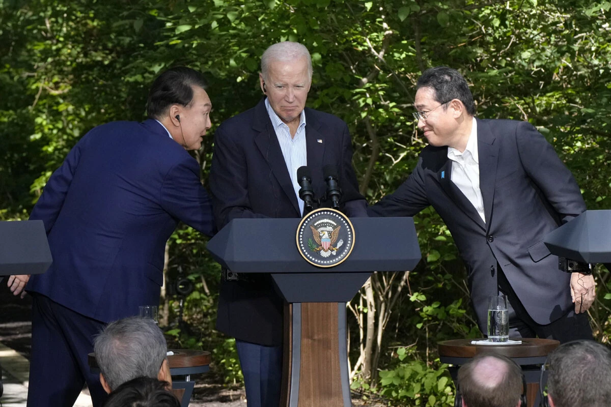 バイデン米大統領を真ん中に、握手する岸田首相とユン韓国大統領。講演台に隠れて見えていないが、本当は握手していないのかもしれない(写真:共同)