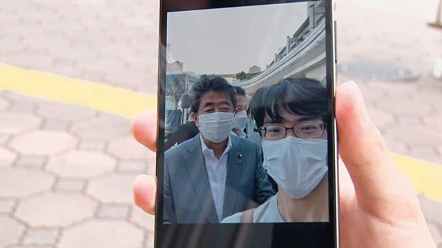 奈良の銃撃現場を訪れていた大学生は、安倍元首相とのツーショット写真を見せ、「突然いなくなってしまって悲しい」と語る。 ©「国葬の日」製作委員会