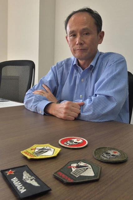 取材に答える山田元空将。机上のパッチは一番上がAGRパイロットを現すスカル（髑髏）で、赤星は旧ソ連をイメージしている。そして真ん中は地上管制官を表すコブラ（毒蛇）。下がウイングマーク