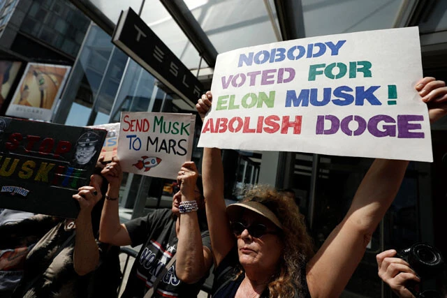 右のプラカードには「誰もイーロン・マスクには投票していない。DOGE（政府効率化省）を廃止せよ」、左のプラカードには「マスクを火星へ送れ」とそれぞれ書いてある
