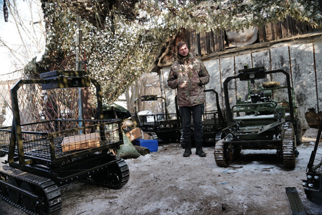 迷彩ネットの下に並ぶUGV（無人地上車両）。台車にキャタピラをつけたような簡素な造りだが実戦で活躍中。金属フレームにはカメラを搭載。バッテリー駆動の電動式で、最大40km走る。スターリンクにつなげばFPVドローンの電波中継車にもなる