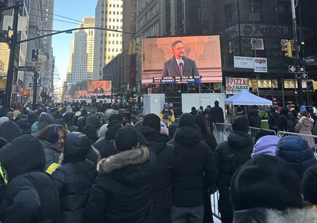 今年1月1日、米ニューヨーク市庁舎で就任演説を行なったマムダニ市長。周辺の路上でその中継画面を見つめるニューヨーカーたち