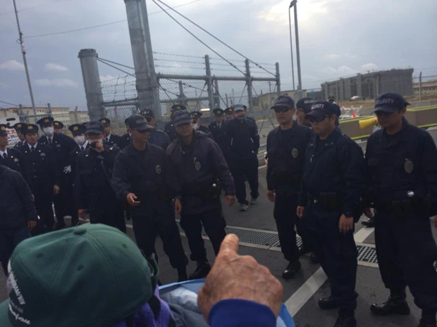 沖縄平和運動センター議長の山城氏が背後から引き倒されて拘束される直前のシーン。異変に気づいた抗議行動の参加者(指さしている人)がとっさに撮影したもの。黒ずくめの5、6名の男がこの直後に山城氏(左の帽子)に襲いかかった