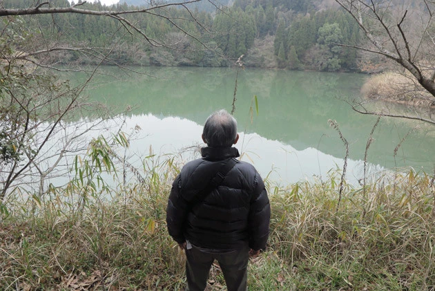 Bさんと共に集落を訪れてみると、引っ越す前には水が抜かれて干上がっていた溜め池の水位はすっかり元に戻っていた(手前はBさん)