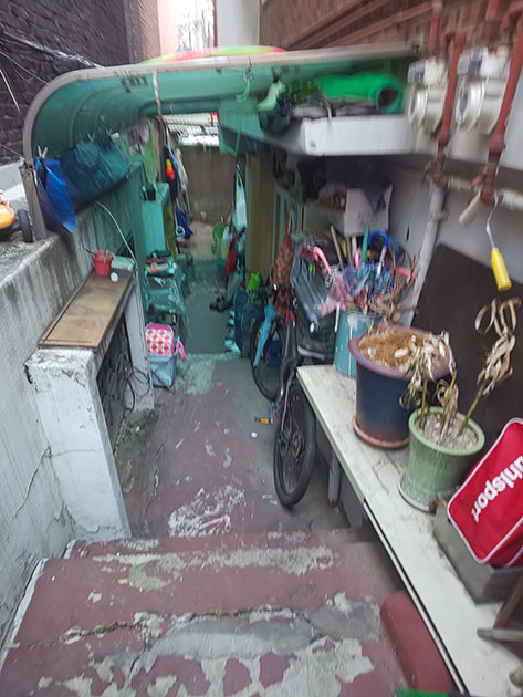 半地下の入り口通路の一例。段々になっている細い道に、植木鉢や子供用の自転車などが並べられている。ここに洗濯物も干すようだ