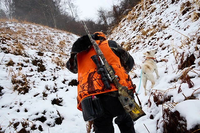 雨の降る雪山に猟犬(写真右側の白い犬)と一緒に入っていく谷島さん。実際はかなりの急斜面だ