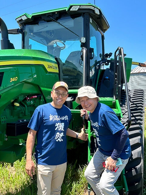 アーカンソー州の田んぼで使っていた巨大トラクターと豊永社長（右）。日本の水田用とは桁違いの340馬力を誇る（本人提供）