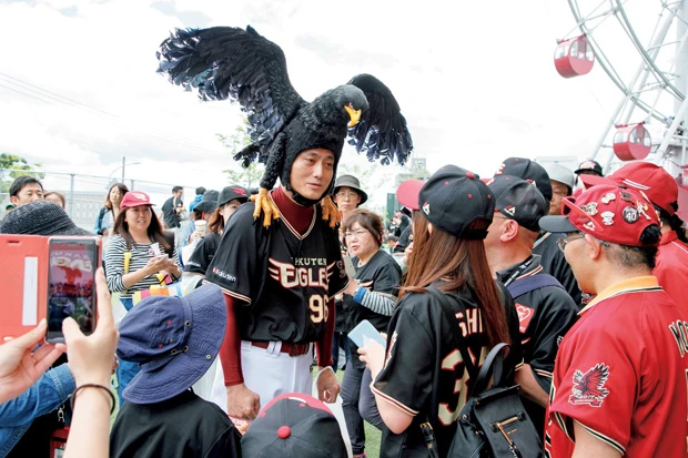  球場の周りでファンに囲まれるクロワシさん。ほとんど言葉を発しないが、記念撮影も気軽に応じてくれ、お願いすれば誰でも名刺がもらえる