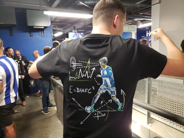 三笘の「ドリブルをテーマにした卒業論文」をモチーフにしたTシャツを着るサポーター