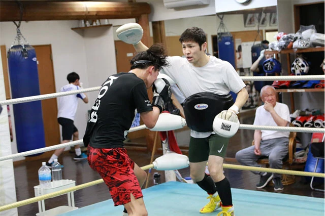 腰にボディミットを装着し、若い練習生相手に指導するユーリ阿久井