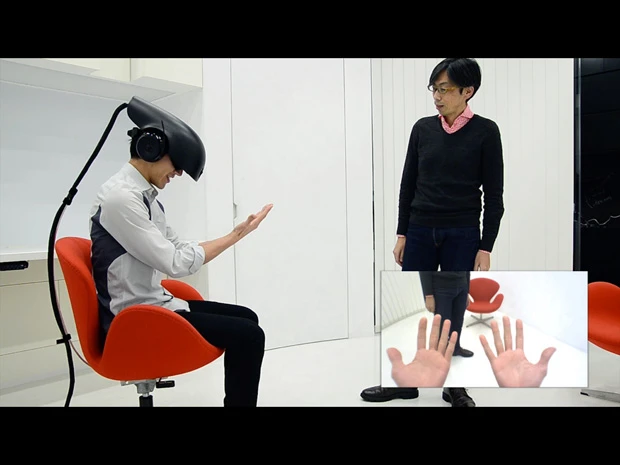 藤井氏（右）によるＳＲ実験の映像。被験者（左）のＨＭＤには実際の映像と過去映像が入り交じって映し出され、「何が現実なのかわからない」状態になって自分の手を見る（右下の枠内が被験者の見ている映像）