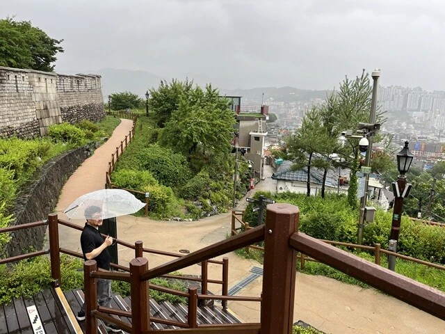 雨の中、ビニール傘を片手に駱山公園を散策するナム。雨天であるからして、見晴らしがいいはずがない。ただ黙々と、公園をぐるっと囲む城壁の周りを歩いた。城壁や公園の所以をナムは丁寧に解説してくれたはずのだが、吹き付ける風でよく聴こえなかった。それに加えて、普段こんなに歩くことのない私は、「登山が趣味」というナムのペースについていくのに精一杯で、ほとんど頭に入らなかった。